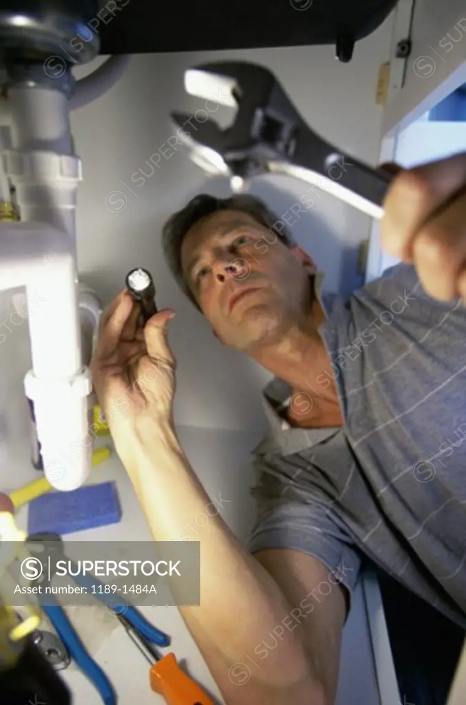 Low angle view of a young man checking the plumbing with a flashlight