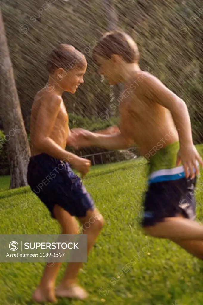 Side profile of two boys playing in a water sprinkler on a lawn