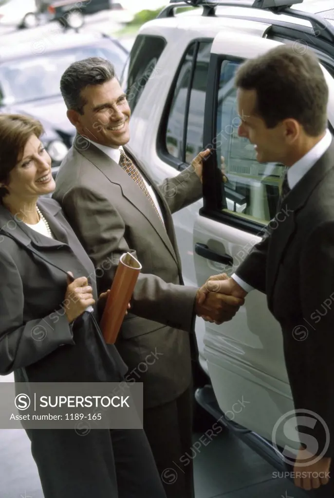 Mature couple shaking hands with a car salesman in a showroom