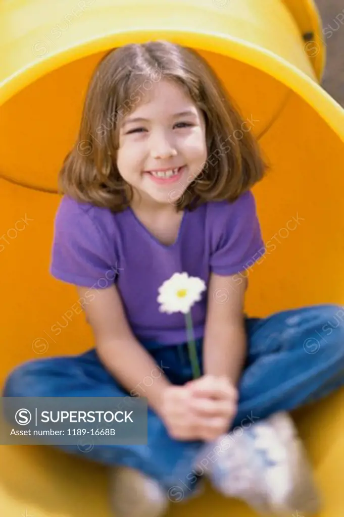 Girl sitting in a pipe and holding a daisy