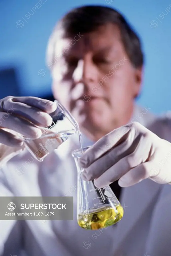Male researcher pouring liquid from a measuring beaker into a conical flask
