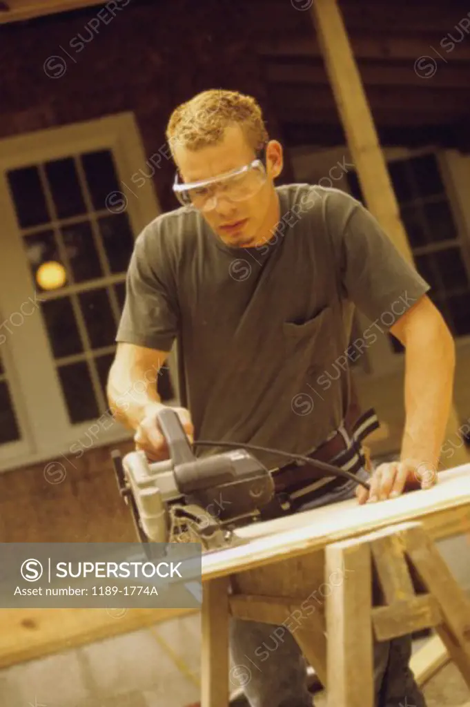 Young man using a power saw on a wooden board