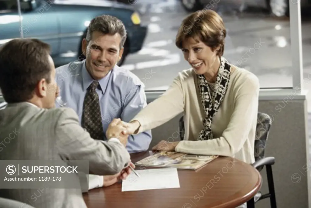 Mature couple shaking hands with a car salesman in a showroom