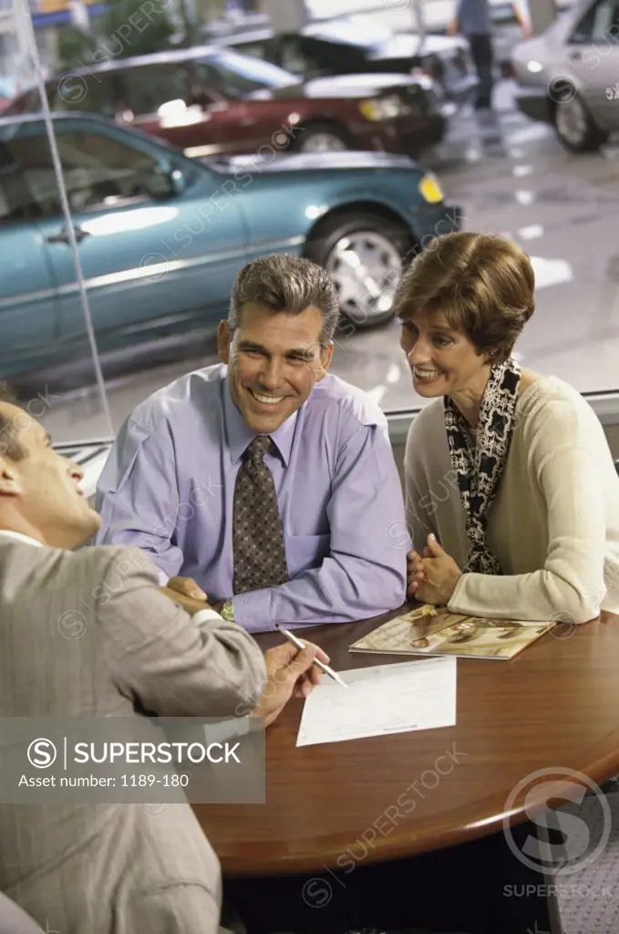 Mature couple shaking hands with a car salesman in a showroom