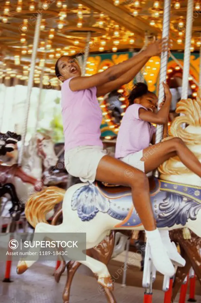 Mid adult woman with her daughter riding a carousel horse