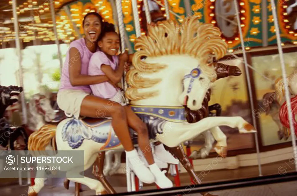 Portrait of a mother and daughter riding on a carousel horse