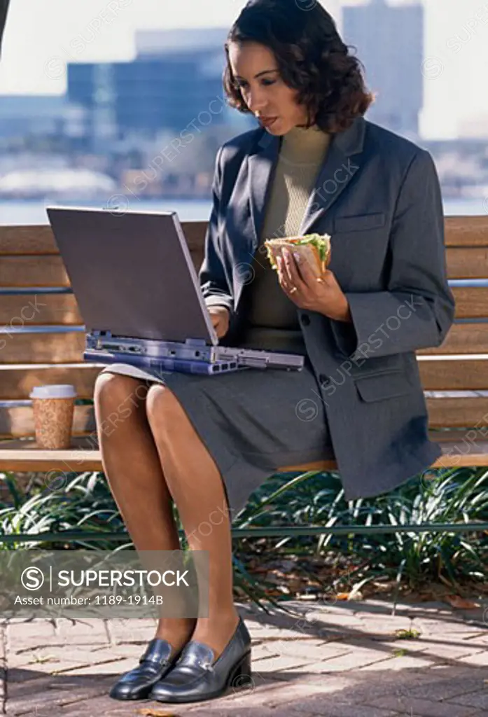 Businesswoman using a laptop and holding a sandwich