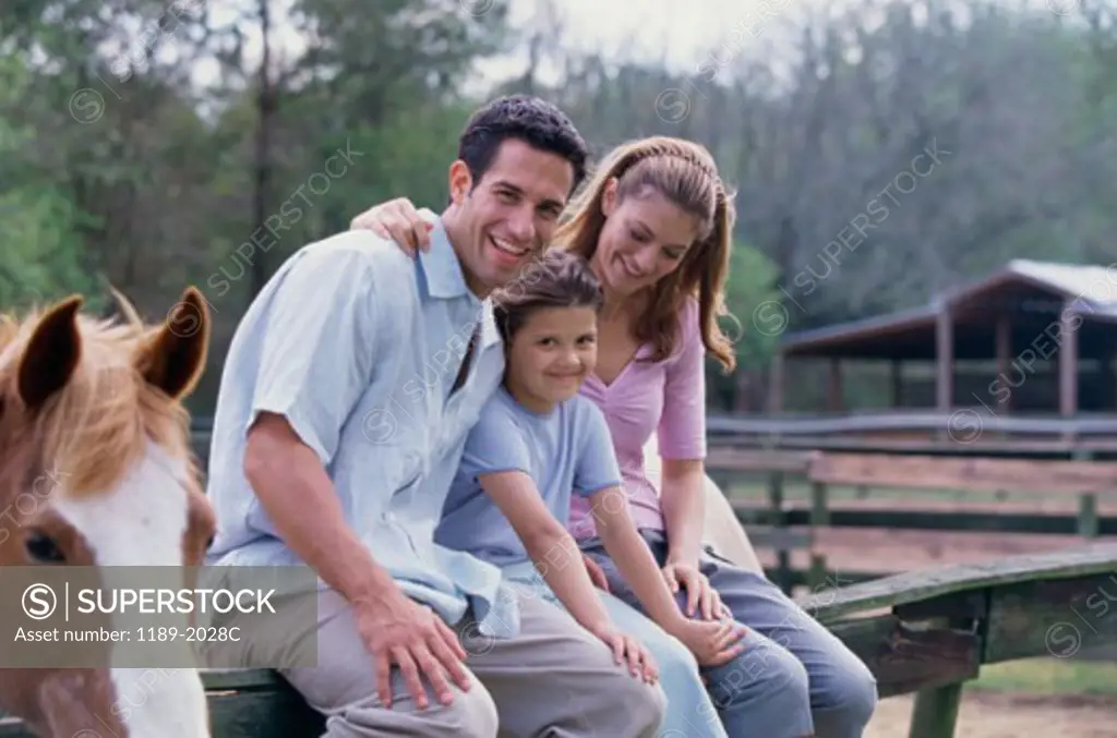 Mid adult couple with their daughter sitting on the fence of a stable