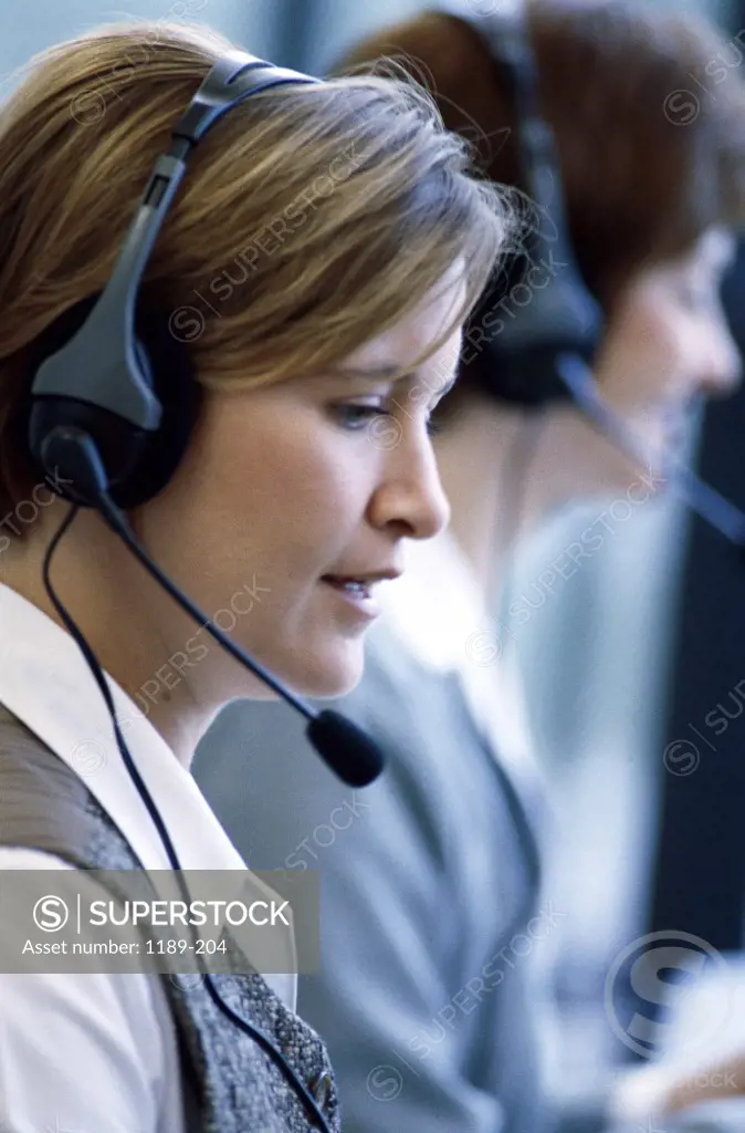 Side profile of two businesswomen wearing headsets working on computers