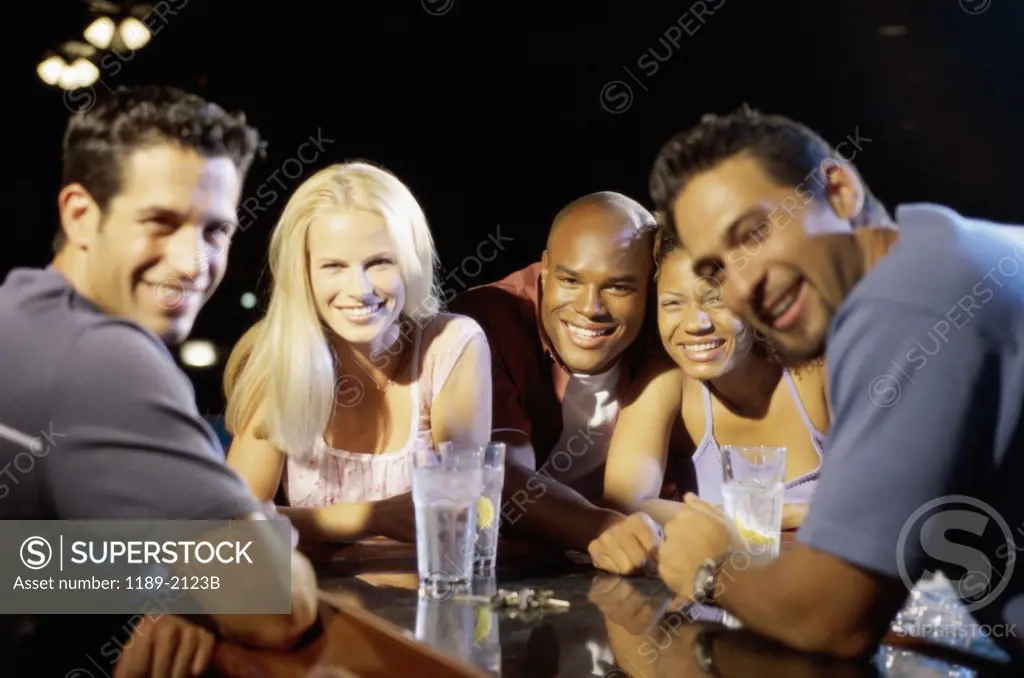 Young man and his friends leaning on a bar counter in a bar and smiling
