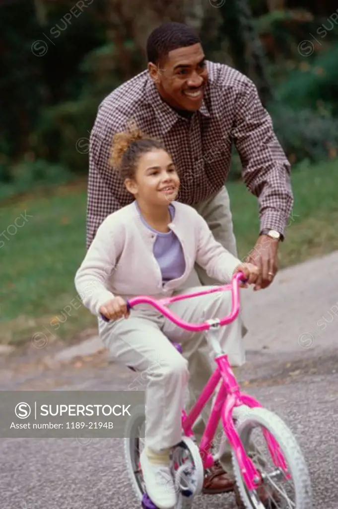 Mid adult man helping his daughter ride a bicycle