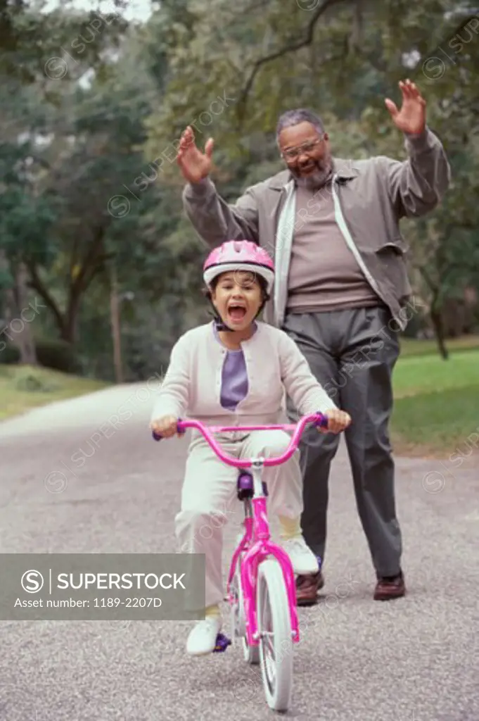 Girl riding a bicycle with her grandfather standing behind her