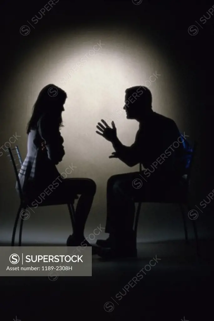 Silhouette of a businessman and a businesswoman sitting face to face arguing