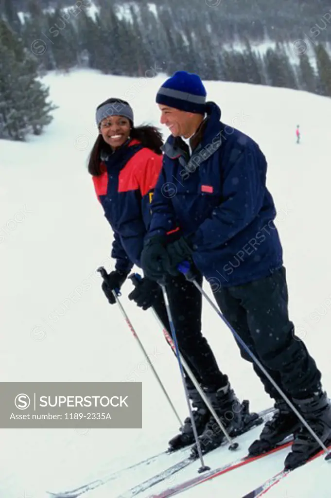 Side profile of a young couple standing in snow with ski equipment