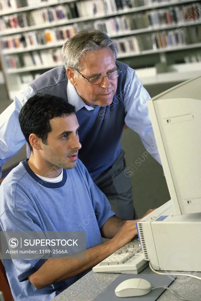 Male teacher with a teenage boy in front of a computer