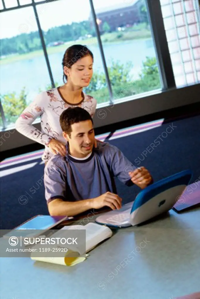 Teenage boy using a laptop with a teenage girl standing behind him