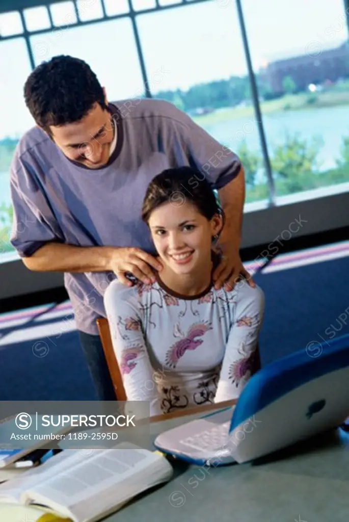 Teenage girl using a laptop with a teenage boy standing behind her