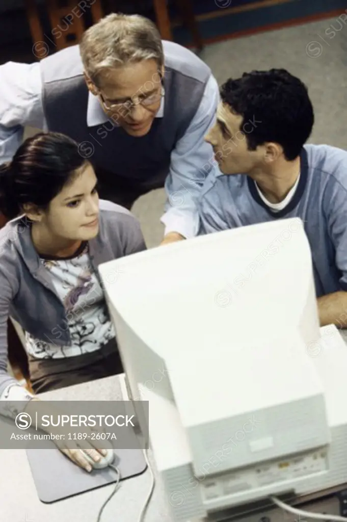 Male teacher with a teenage boy and a teenage girl in front of a computer
