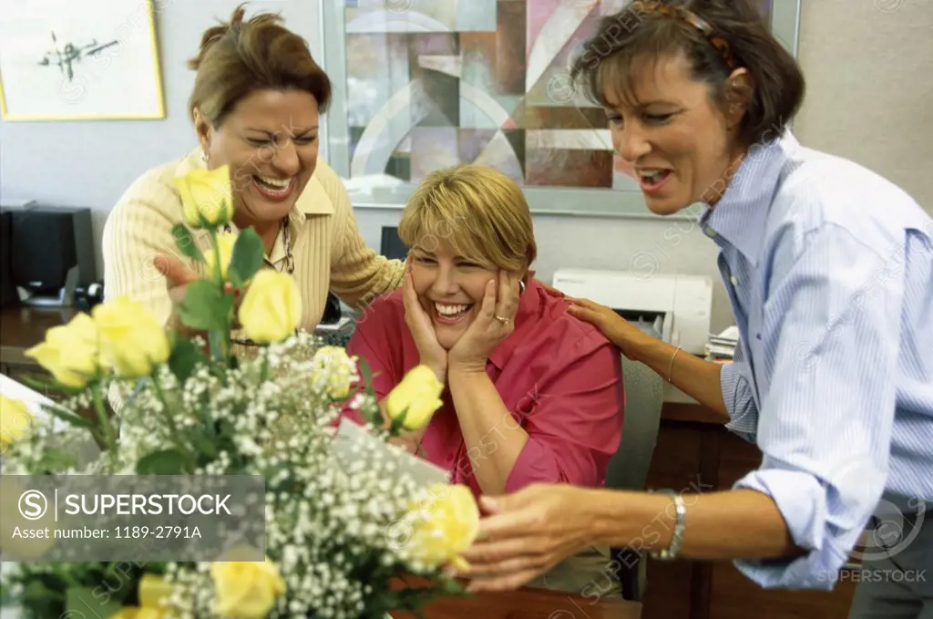 Three businesswomen looking at a bouquet of flowers in an office