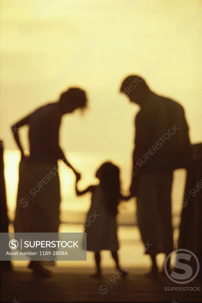 Silhouette of a young couple with their daughter on the beach