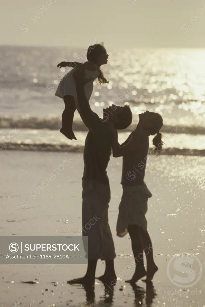 Silhouette of a young couple on the beach with their daughter
