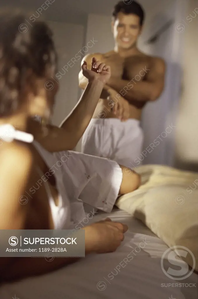 Young woman lying in bed and gesturing to a young man