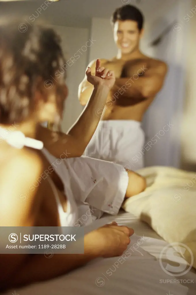 Young woman lying in bed and gesturing to a young man