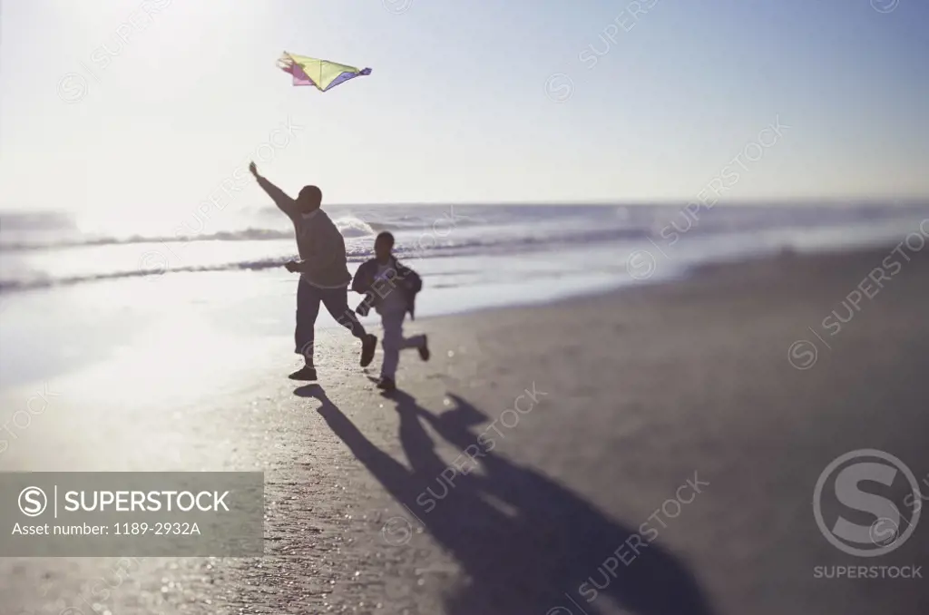 Silhouette of a father and his son running on the beach flying a kite