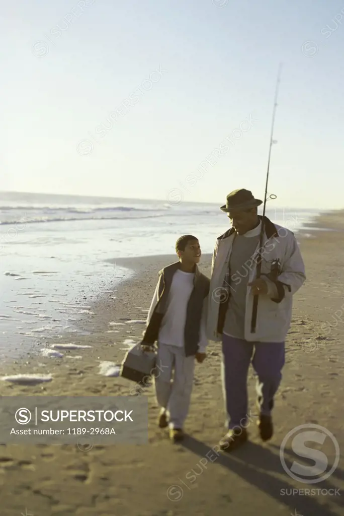 Father and his son walking on the beach with fishing gear