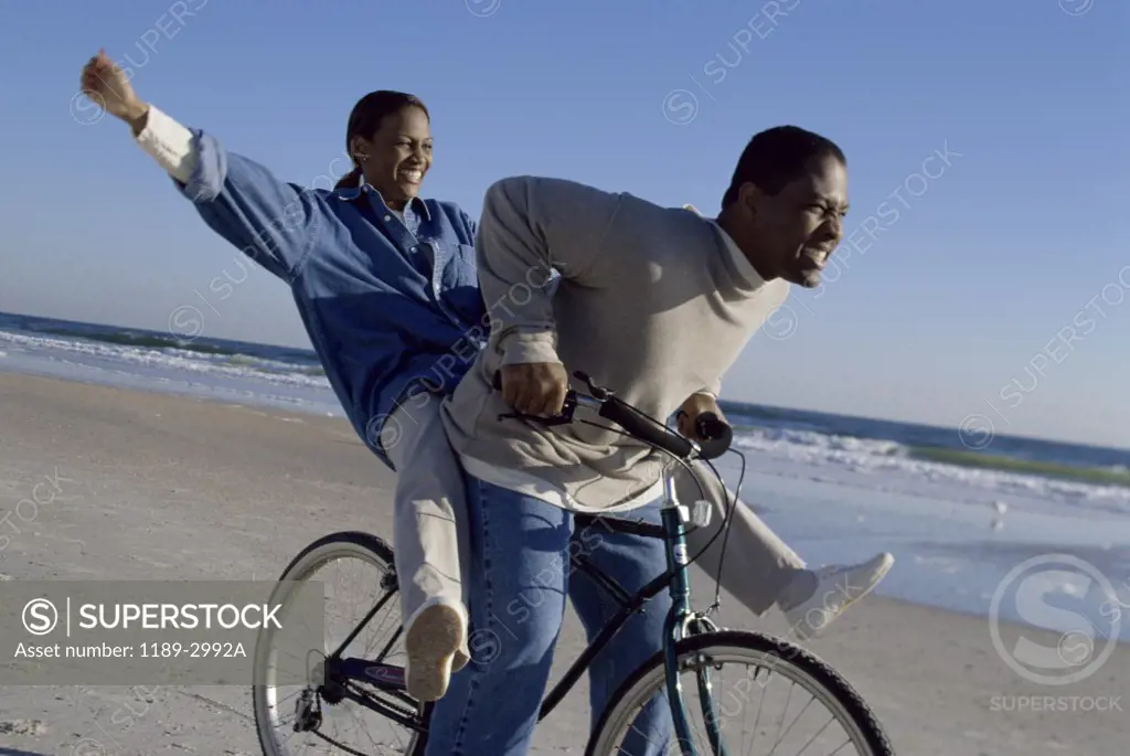 Side profile of a young couple riding a bicycle on the beach