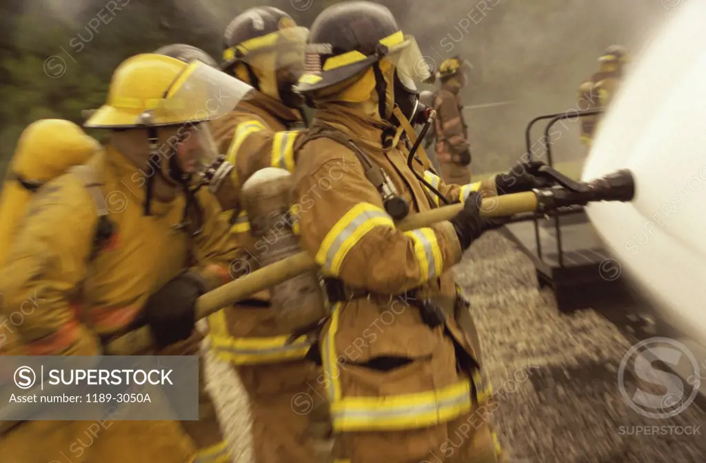 Side profile of a group of firefighters holding water hoses