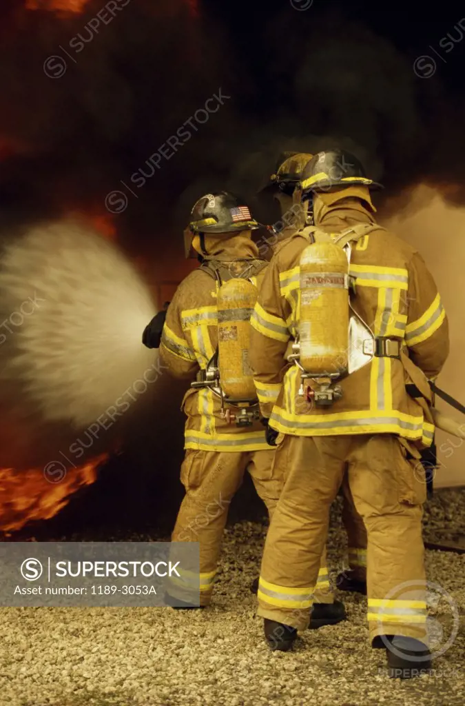 Rear view of three firefighters extinguishing a fire