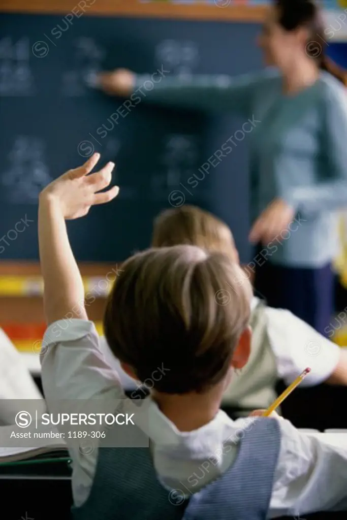 Rear view of a schoolgirl raising her hand in a classroom
