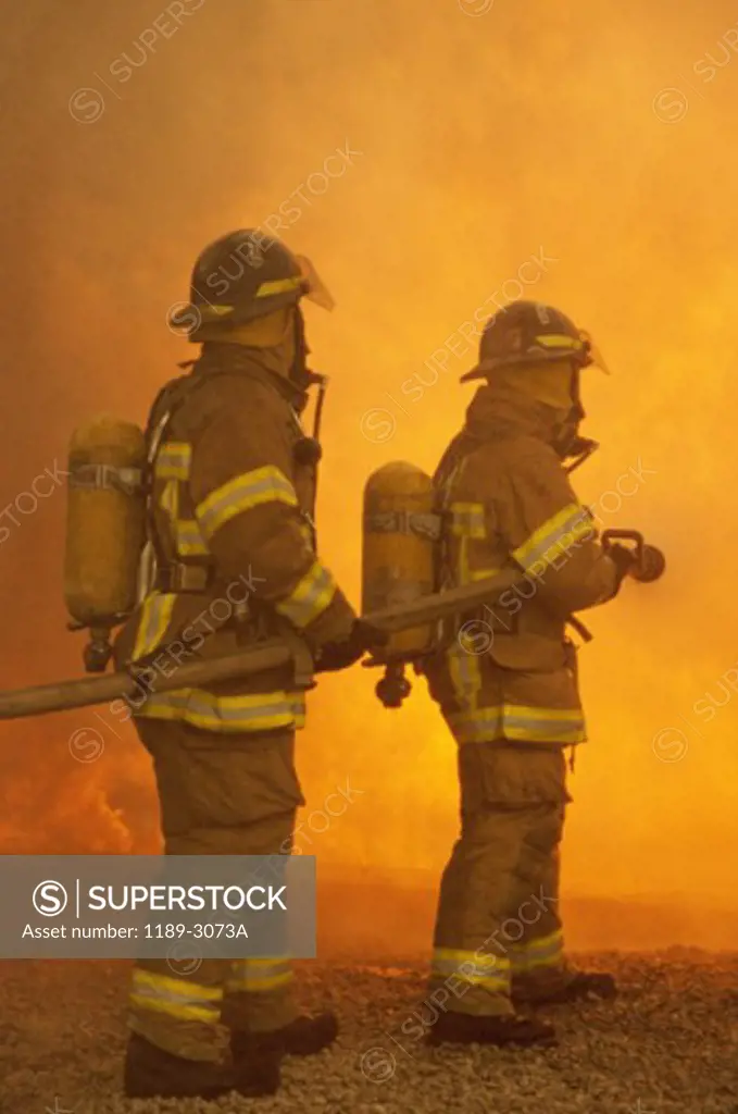 Rear view of two firefighters extinguishing a fire