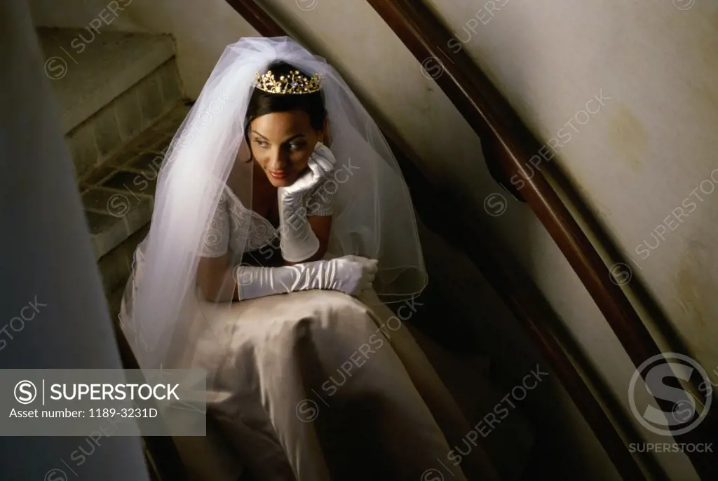 Bride sitting on a staircase with her hand on her chin