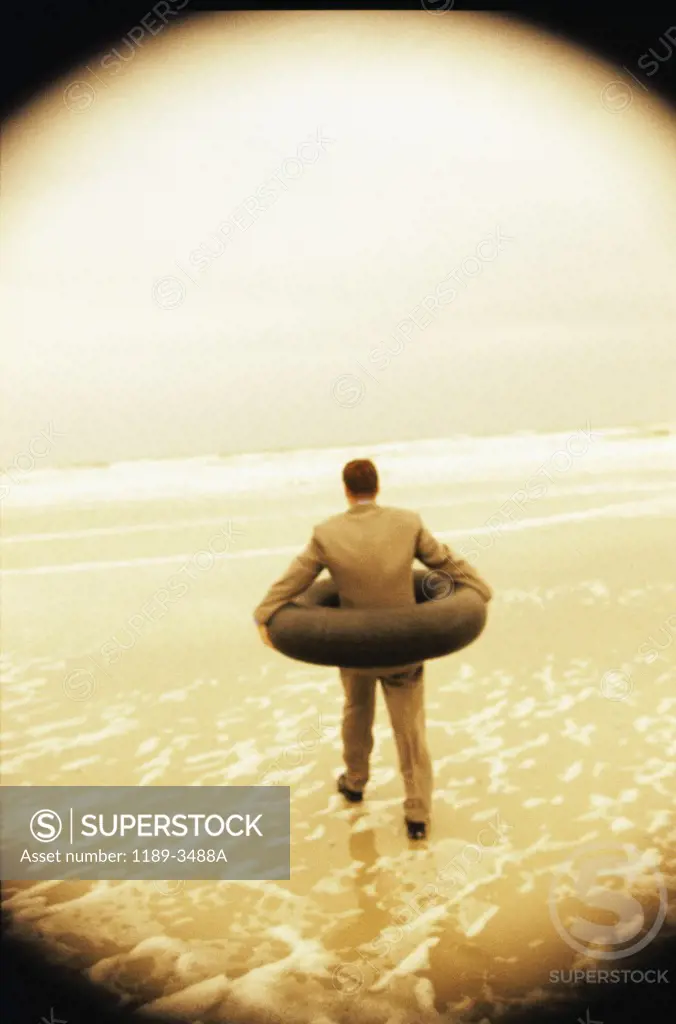 Rear view of a businessman wearing an inner tube around him at the beach