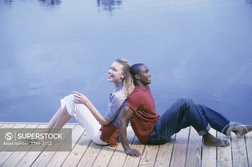 Young couple sitting back to back beside a lake
