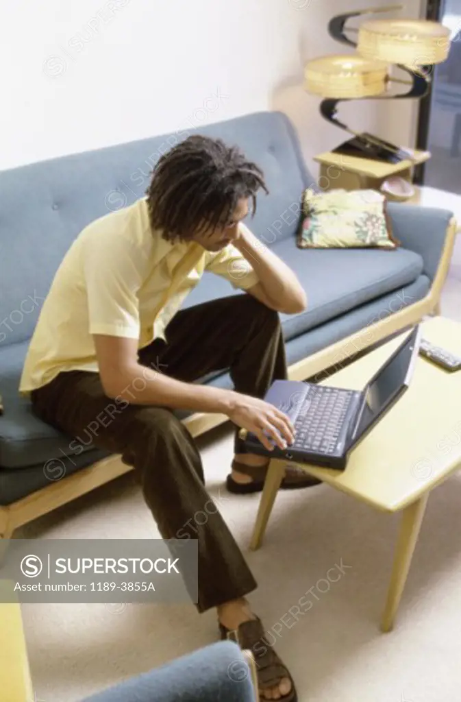 High angle view of a young man sitting on a couch using a laptop