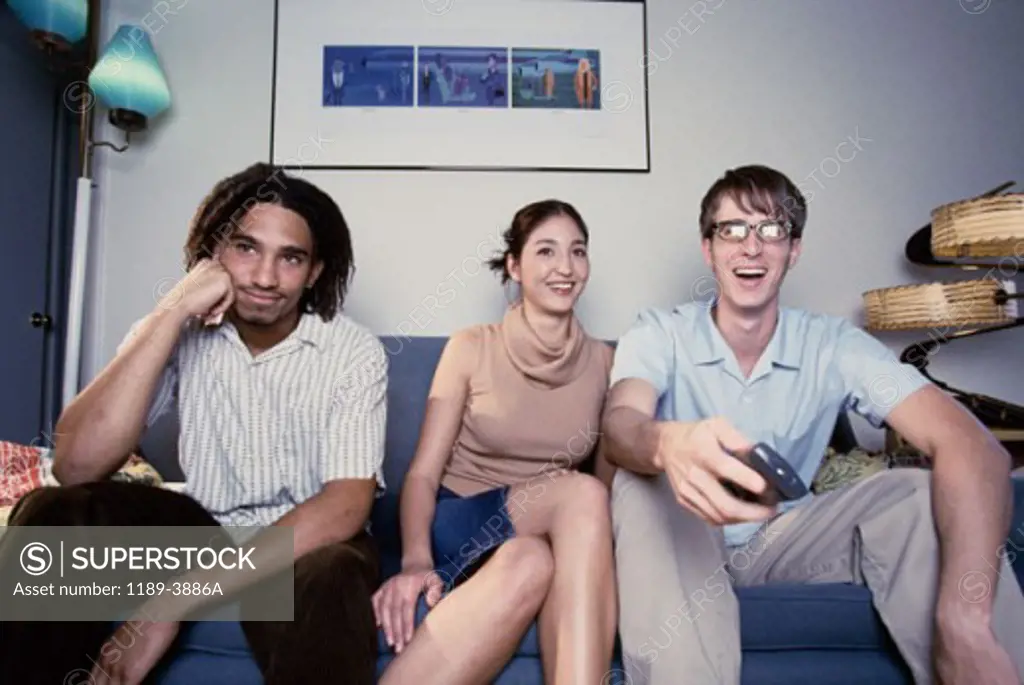 Two young men and a young woman sitting together on a couch and watching television