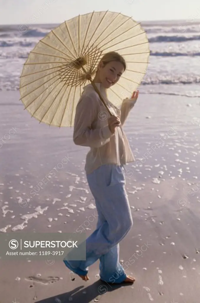 Portrait of a young woman walking on the beach with an umbrella