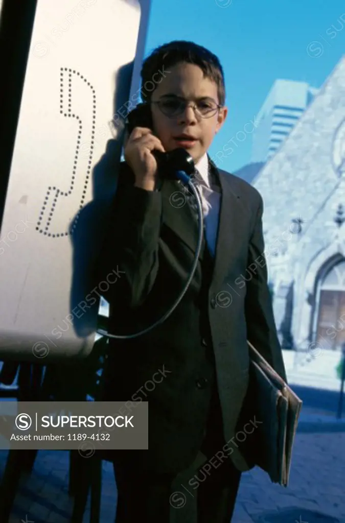 Portrait of a boy wearing a business suit talking on a pay phone