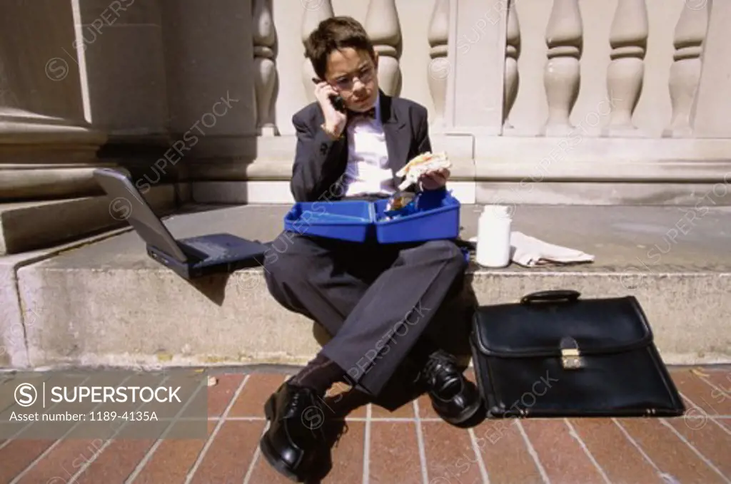 Boy wearing a business suit sitting on a step holding a lunch box