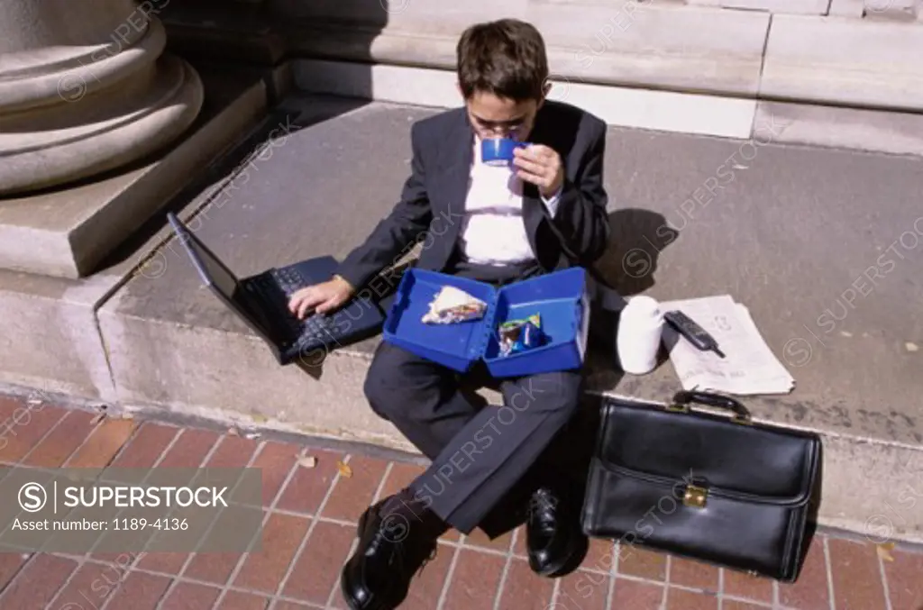High angle view of a boy wearing a business suit sitting on a step holding a lunch box
