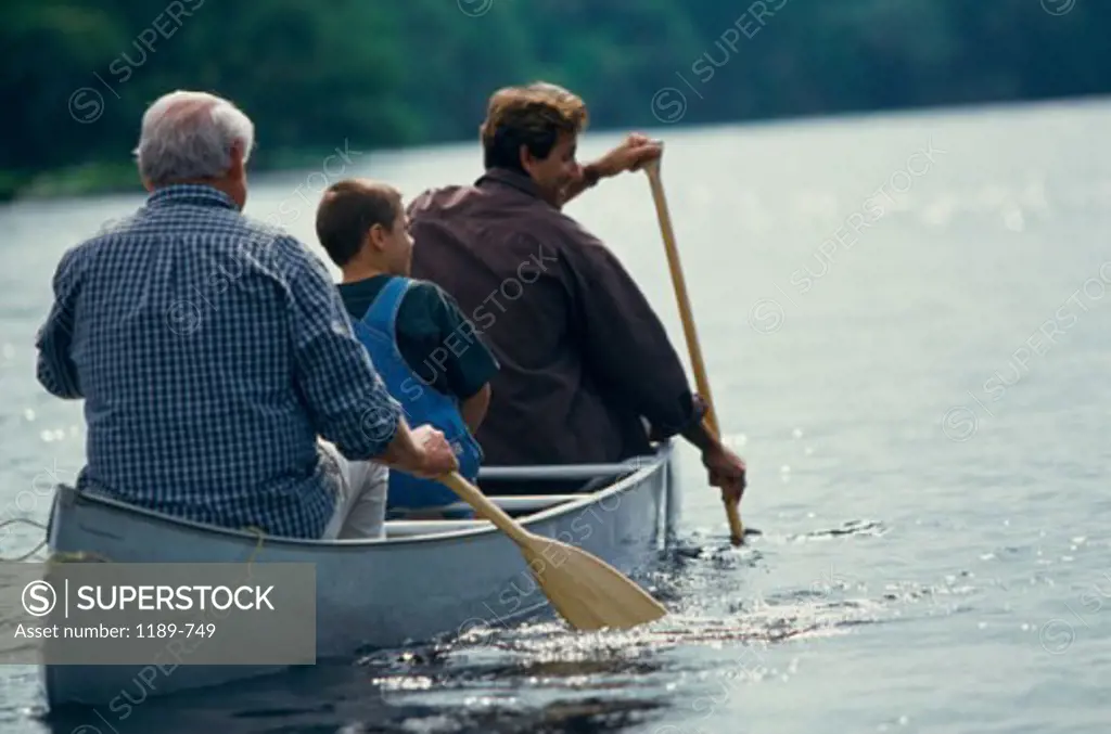 Rear view of a grandfather rowing a boat with his son and grandson in a lake