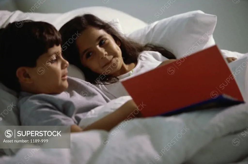 Boy and a girl lying in bed reading a book