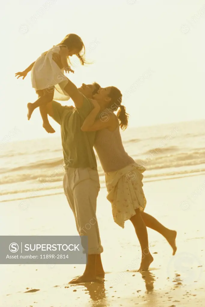 Father and mother playing with their daughter on the beach