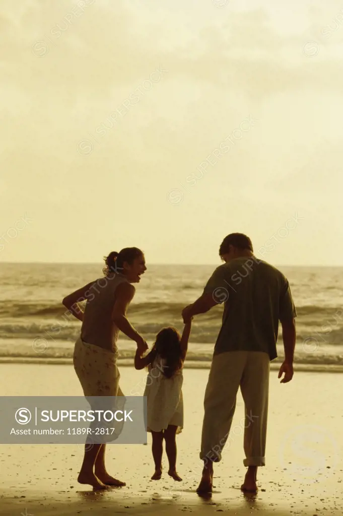 Rear view of a father and mother with their daughter on the beach