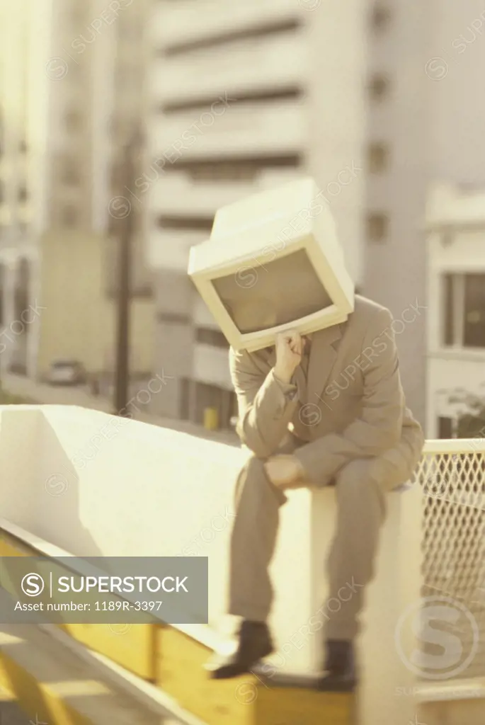 Businessman sitting on a wall with computer monitor for a head