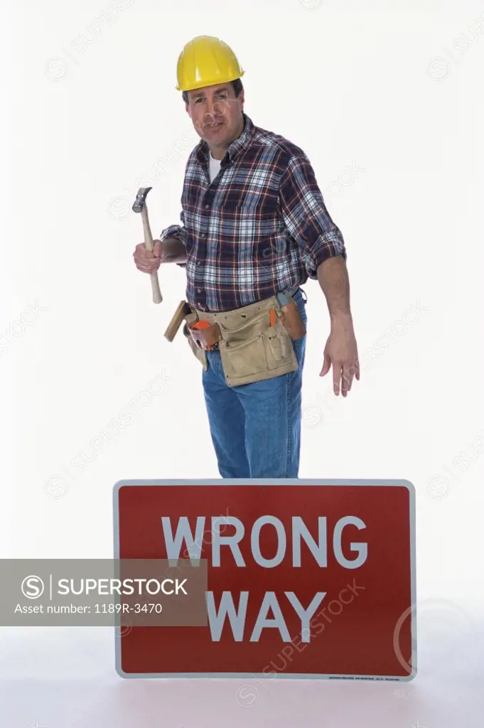 Portrait of a worker holding a hammer standing next to a wrong way sign