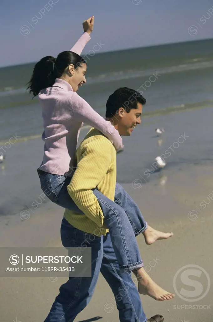 Young woman riding piggyback on a young man at the beach